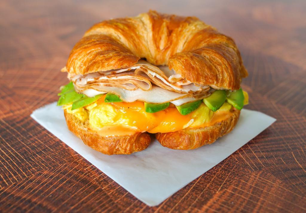 Croissant, Smoked Turkey, Avocado, Egg, & Cheddar Sandwich · 2 scrambled eggs, melted Cheddar cheese, sliced smoked turkey, avocado, and Sriracha aioli on a warm croissant.