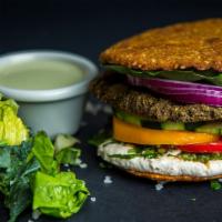 Falafel Burger · Vegan. Crunchy almond, sunflower seed falafel burger with hummus, parsley, onion, tomato, pi...