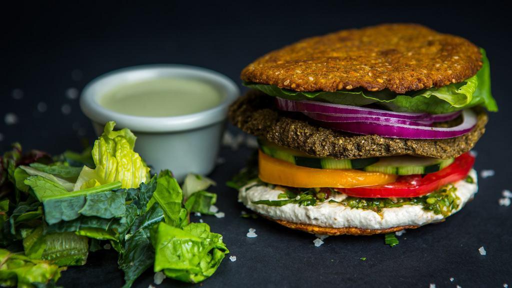 Falafel Burger · Vegan. Crunchy almond, sunflower seed falafel burger with hummus, parsley, onion, tomato, pickle, and romaine lettuce sandwiched in our baked buckwheat bun. Served with a side salad and tahini blueberry vinaigrette dressing.