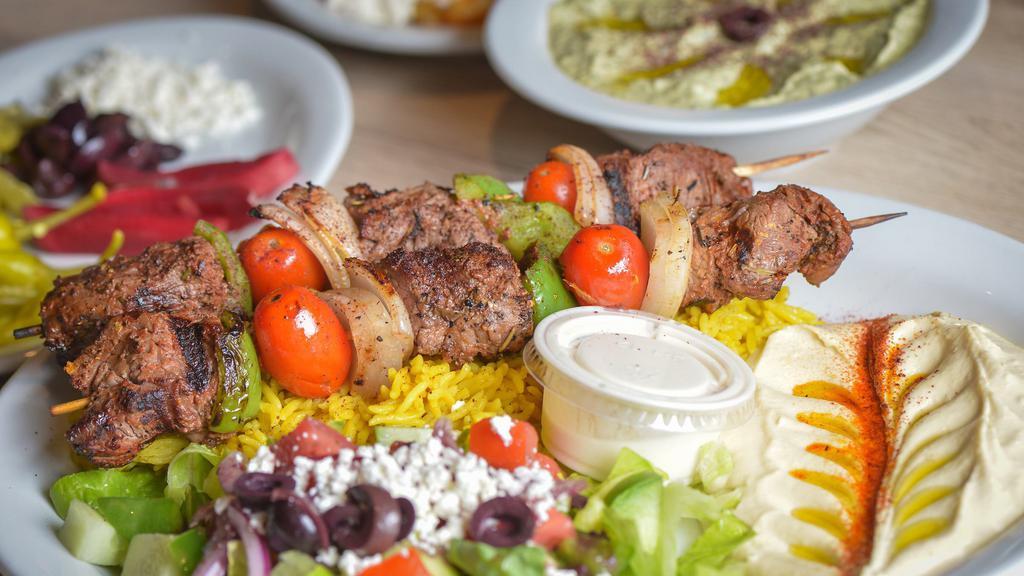 Beef Shish Kabab (Tekka) Plate · Two skewers of beef kabab style, served with grilled green peppers and tomatoes, rice, Greek salad, hummus, pita bread, and tahini sauce.