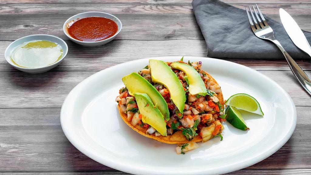 Tostada De Fish Ceviche · Fresh white fish marinated in lime juice mixed with cilantro, chopped onions and diced carrots. Topped with avocado slices.