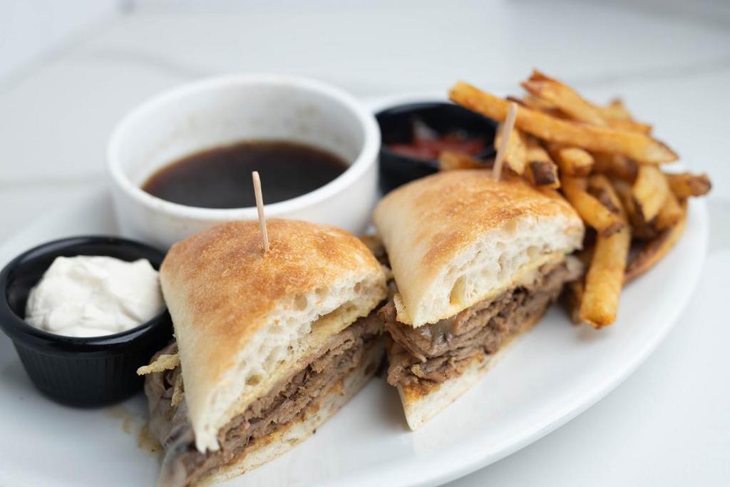 French Dip Sandwich · Slow roasted, thinly sliced beef tip topped with melted provolone cheese piled high on a Parmesan grilled ciabatta bun and served with a side of horseradish cream and Rosemary Au Jus.