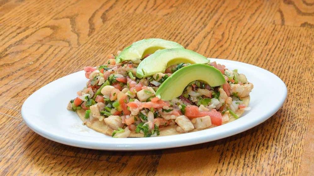 Ceviche Tostada · White fish, onions, tomatoes, cilantro, and jalapenos marinated in lime juice on a crispy corn tortilla, and topped with avocado.
