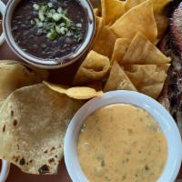 Plato Tejano (Brisket) · Sliced smoked brisket with refried black beans, tortillas, chips, salsa, and queso