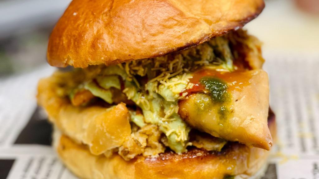 O.B. (Samosa On A Bun) · Two Samosas smashed in between a Local Baked Bun. Topped with Raita Sauce, Red Chile Garlic Chutney, Sweet and Sour Tamarind Chutney, Cilantro-Mint Chutney, Onions and Cucumber.