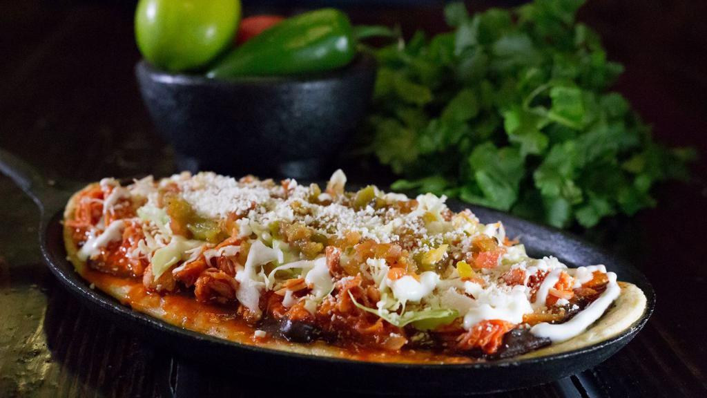 Huarache Asada (Handmade Of Corn And  Shaped Like A Mexican Sandal) · Huarache: spread with black beans topped with Asada, cabbage, sour cream and cotija cheese.
(Hurache de Asada con frijoles negros, repollo, crema y cotija).