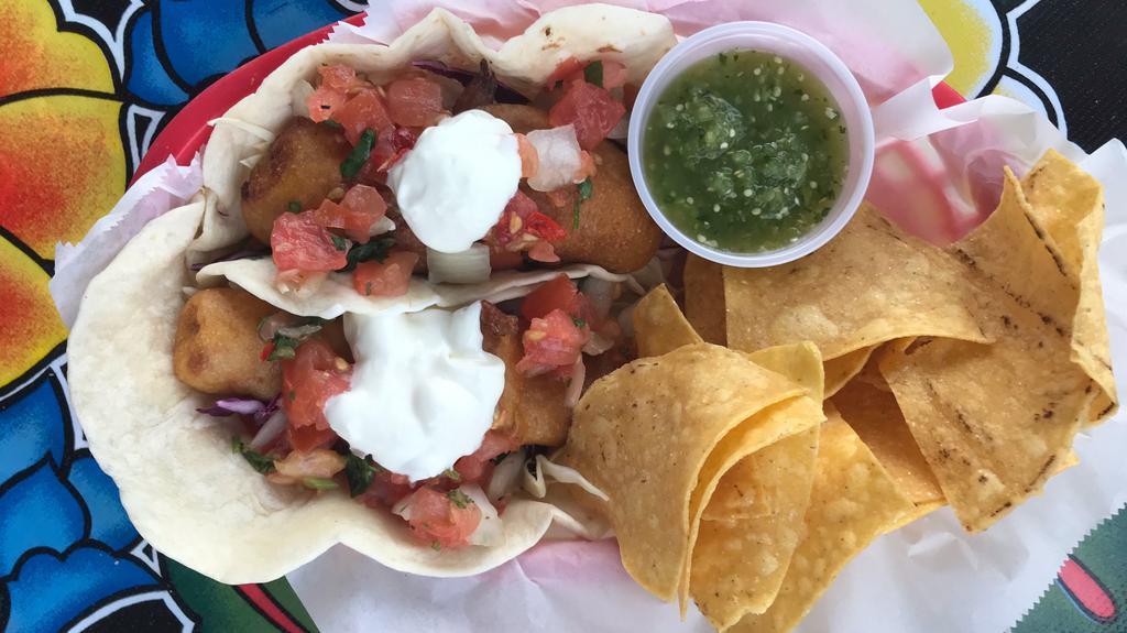 Beer Battered Cod Tacos · Pacific cod fried in a cornmeal beer batter. Topped with shredded cabbage, pico de gallo, crema agria, and a squeeze o'lime. Served with a handful of chips and a side of salsa.
