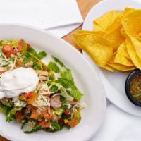 Grilled Chicken Tostada Salad · Grilled chicken layered with a small crispy corn tortilla, black beans, romaine lettuce, pic...