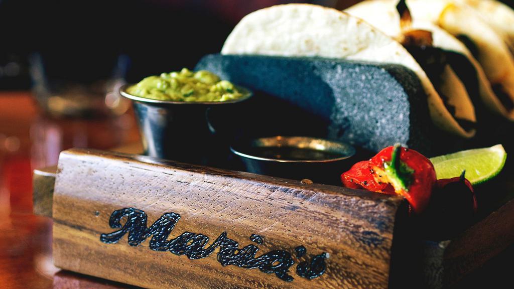 Tacos De Alambre · Three flour tortillas filled with strips of marinated steak, sautéed bell peppers, onions, topped with melted manchego cheese and guacamole. Side of fire roasted tomatillo salsa, served in a stone taco holder.