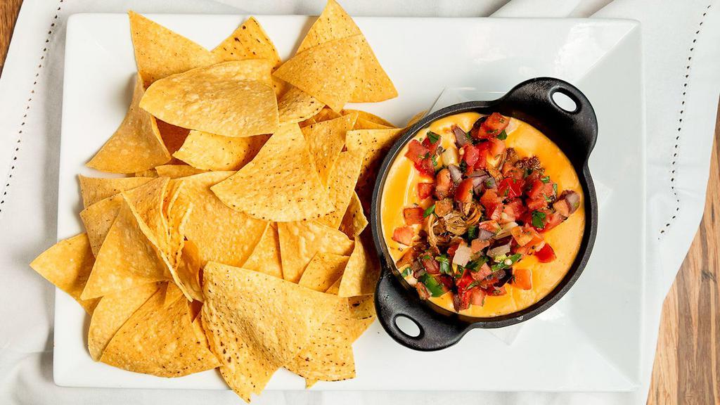 Carnitas Queso · Housemade spicy queso topped with tender pork and garnished with pico de gallo. Choice of toasted crostinis or tortilla chips.