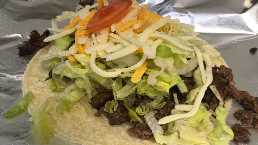 Carne Asada Taco · A burrito that is filled with carne asada, beans, lettuce, cheese, & tomato, on a corn tortilla