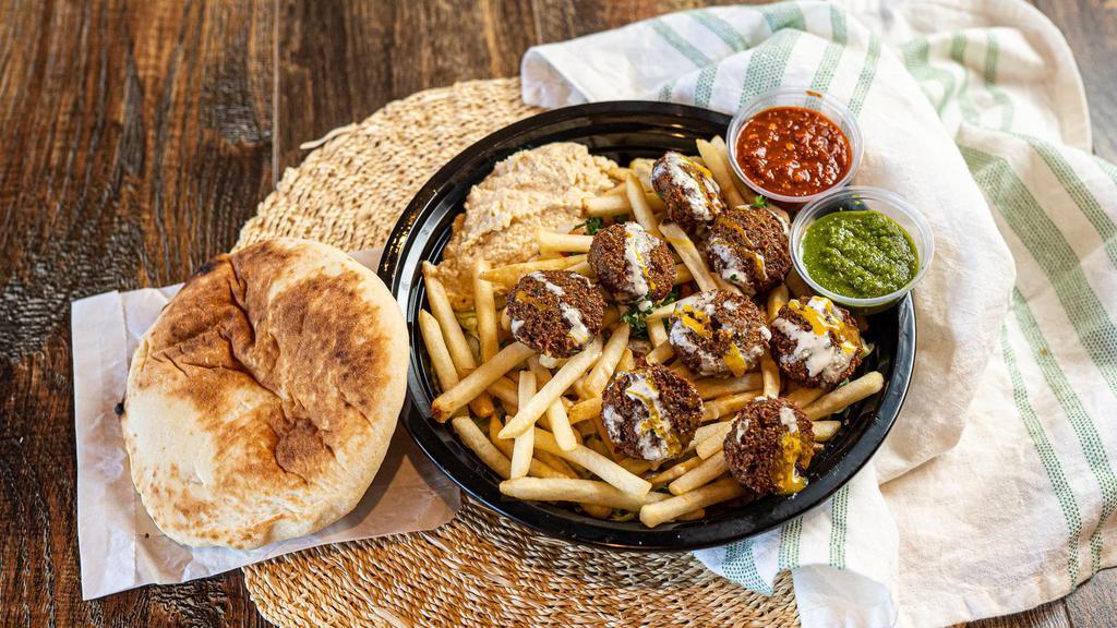 Falafel Fries · Eight falafel balls on top of crispy fries drizzled with tahini on a bed of salad with olive oil, lemon, hummus, and a fresh pita on the side.