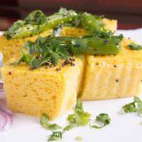 Khaman Dhokla · Yellow cake steamed, made from gram flour, topped with mustard seeds, sesame seeds and chill...