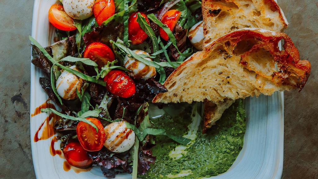 The Biz Caprese · House-made vegan pesto + mozzarella, tomato, red onion, sprouts & balsamic glaze; served with garlic toast on a bed of mixed greens