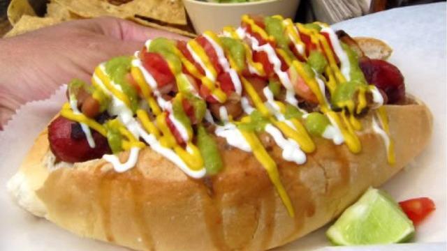 Sonoran Dog Hot · Hot dog Bun, Grilled Onions, Pinto Beans, Bacon, Avocado Spread, Mayo, & Tomato.