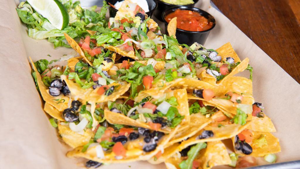 Ale House Nachos · Crispy tortilla chips with melted cheddar and pepper jack cheeses. Topped with black beans, roasted corn, avocado, onion salsa, romaine, green onions, cilantro, sour cream, salsa, and tomatoes. Served with your choice of chipotle chicken or beef.
