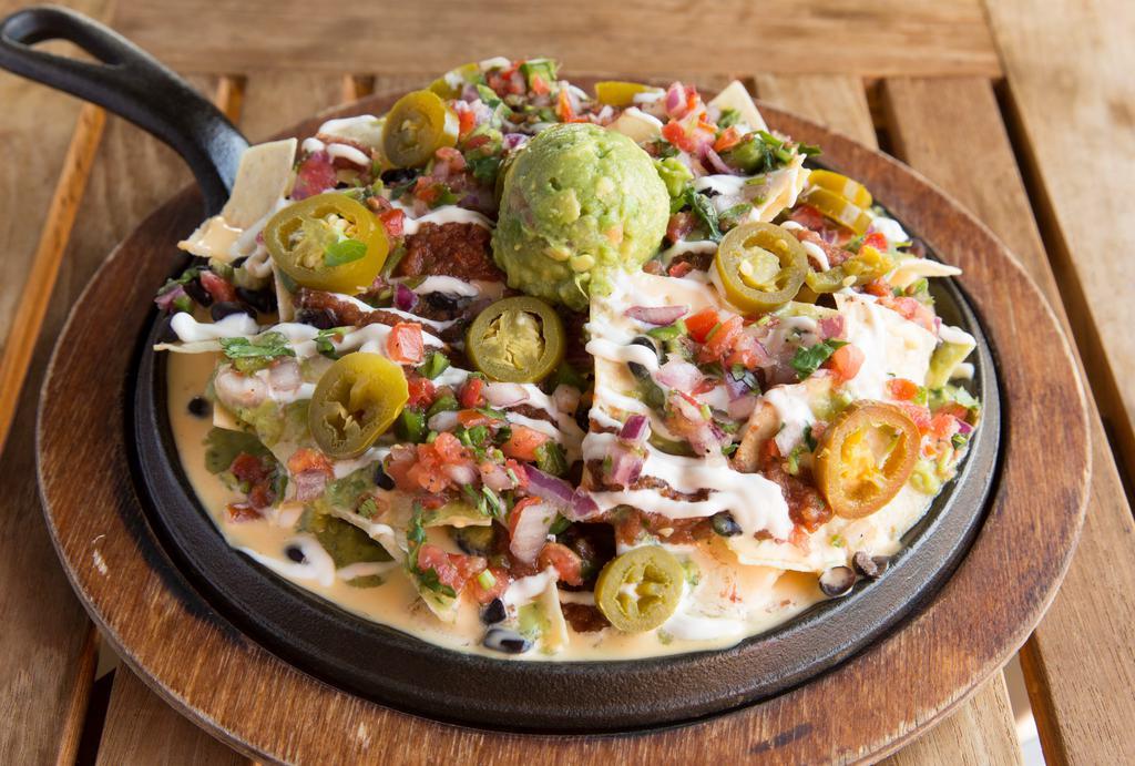 Loaded Vegan Nachos · Crispy corn chips topped with black beans, homemade vegan queso, vegan sour cream, avocado lime salsita, salsa fresca, fresh guacamole and pickled jalapenos. Vegan.