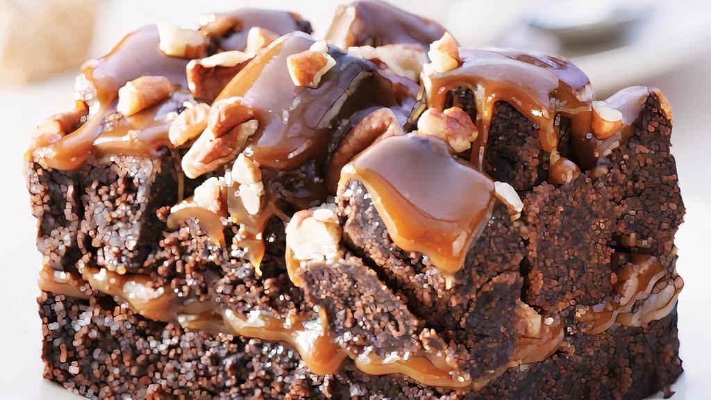 Rockslide Brownie · A light textured Brownie topped with butter-luscious caramel, piled high with Brownie cubes, toasted pecans and drizzle with caramel ganache.