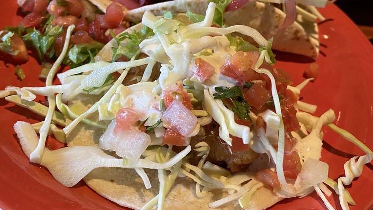 Taco-Pescado · breaded and fried white fish on two corn tortillas topped with salsa fresca, cabbage, pickled onions, and tangy salsa blanca.