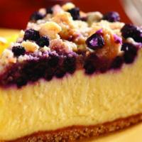 Lemon Blueberry Crumb Cheesecake · A creamy lemon cheesecake topped with blueberries and brown sugar crumbs, sits on a cookie b...