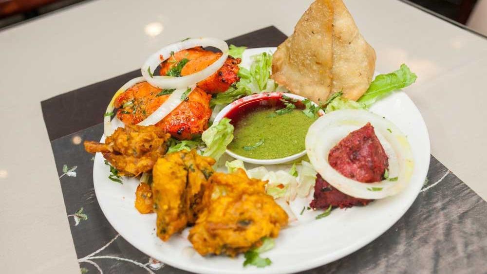 Taste Of India Delight · A selection of vegetable samosa, vegetable pakora, chicken tikka, and chicken pakoras. Served with cilantro and tamarind chutneys.