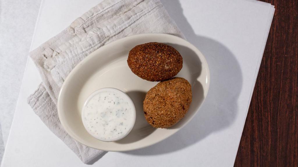 Kibbeh · Beef ground to a fine pate is mixed with cracked wheat. As a meat “dough” it forms two layers encasing a filling of seasoned ground beef, onions and pine nuts. Served with taziki sauce.