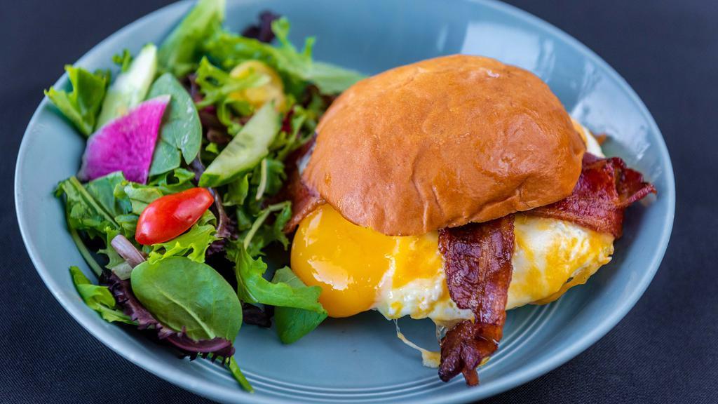 *Brekkie Sandwich · Two sunny-side up farm eggs, applewood smoked bacon, cheddar cheese, kosho aioli, house hawaiian sweet bun, organic greens.