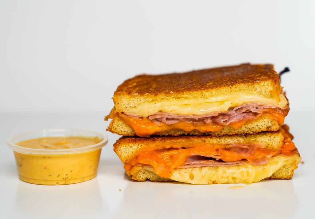 Smoked Ham & Three Cheese Melt · Smoked ham, Cheddar, Swiss, and Parmesan cheeses melted between buttery, toasted sourdough bread. Served with a side of Spicy Honey Mustard Aioli.