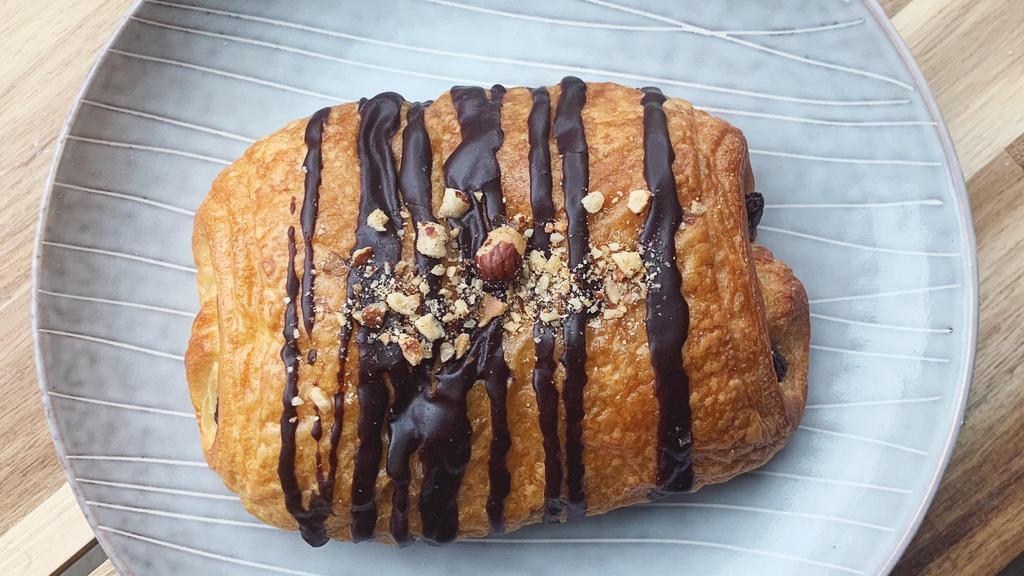 Chocolate Nutella Croissant · Flaky croissant dough filled with dark chocolate & nutella and topped with chocolate glaze & hazelnuts