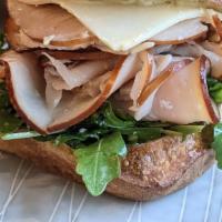 Turkey Ciabatta Sandwich · Roasted turkey, white cheddar, preserved meyer lemon aioli, red onions & arugula tossed in o...