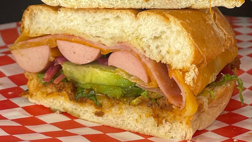 Cubana Torta · sandwich filled with pork, refried beans, onions, tomatoes, chicken hotdogs, cheese, sliced ham, lettuce, avocados and mayonnaise.