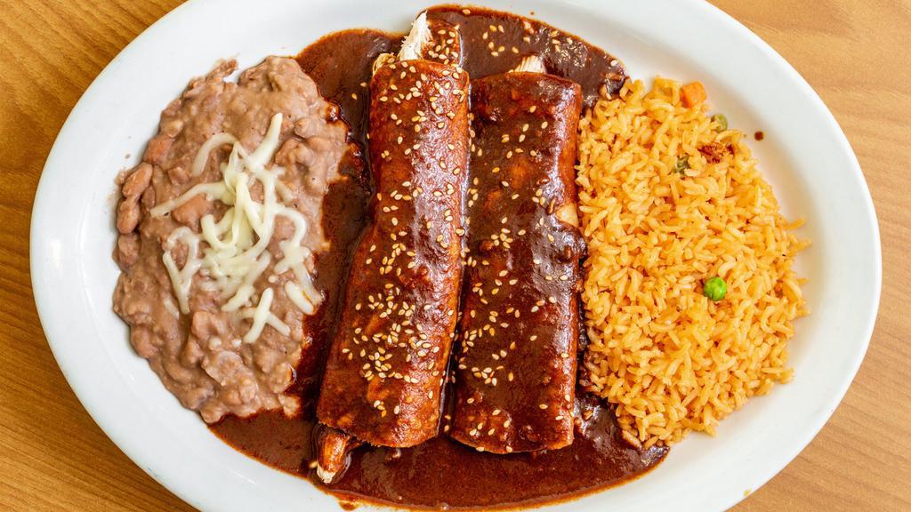 Enchiladas De Mole · 2 corn tortillas smothered in mole sauce filled with meat, topped with mozzarella cheese. Served with rice, salad & refried pinto beans on the side.