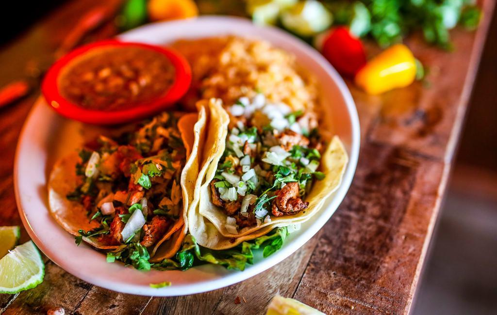 Tacos Al Pastor · Gluten-free. Two soft corn tortillas filled with marinated diced pork, topped with chopped onions and fresh cilantro. Served with charro beans and Mexican rice.