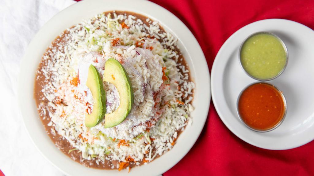 Tostada · Crispy corn tortilla layered with pinto beans, cabbage, shredded carrot, tomatoes, onion, sour cream, cotija cheese, and avocado.