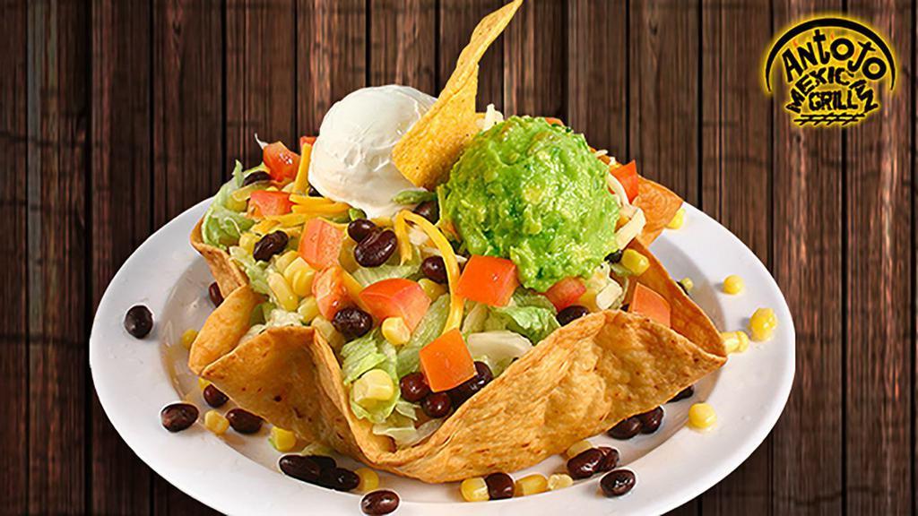 Antojo Taco Salad · With your choice of shredded chicken, shredded beef or ground beef. Both refried and black beans, corn, dice tomatoes, lettuce, shredded cheddar cheese all in a tortilla shell. Topped with sour cream and guacamole.