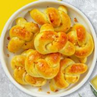 Garlic Knots Unravel  · Our house made pizza dough, knotted up, baked, then smothered in real garlic butter and parm...