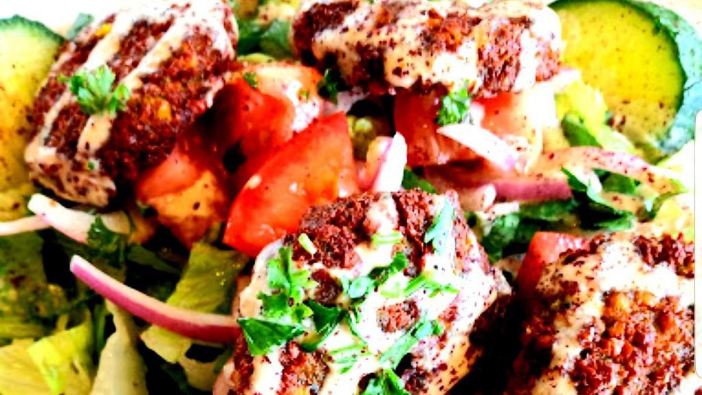 Falafel Salad · Homemade falafel (6 pieces). Staple Middle Eastern dish, crunchy mixture of chickpeas, crisp fresh herbs & spices. Served on a bed of Romaine lettuce, English cucumbers, red onions, tomatoes with Greek dressing and tahini. Garnish with sumac (red citric spice) and fresh chopped parsley.