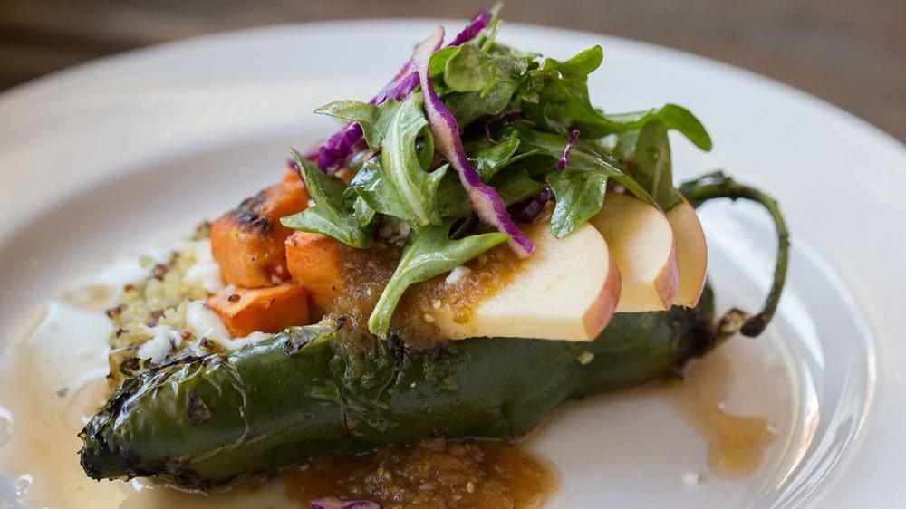 Chile Relleno · A fire-roasted poblano pepper stuffed with quinoa, sweet potato, and apples, topped with queso fresco and ranchero salsa, served with our white garbanzo bean medley and veggies. (hold the cheese = v.