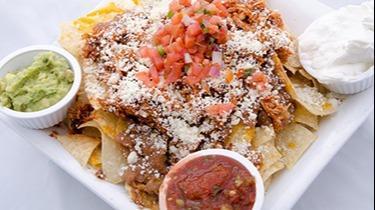 Chipotle Chicken Nachos · Layers of freshly made white corn tortilla chips, cheddar and pepperjack cheeses topped with refied beans, shredded chipotle chicken, fresh pico de gallo and cotija cheese. Served with guacamole and sour cream.