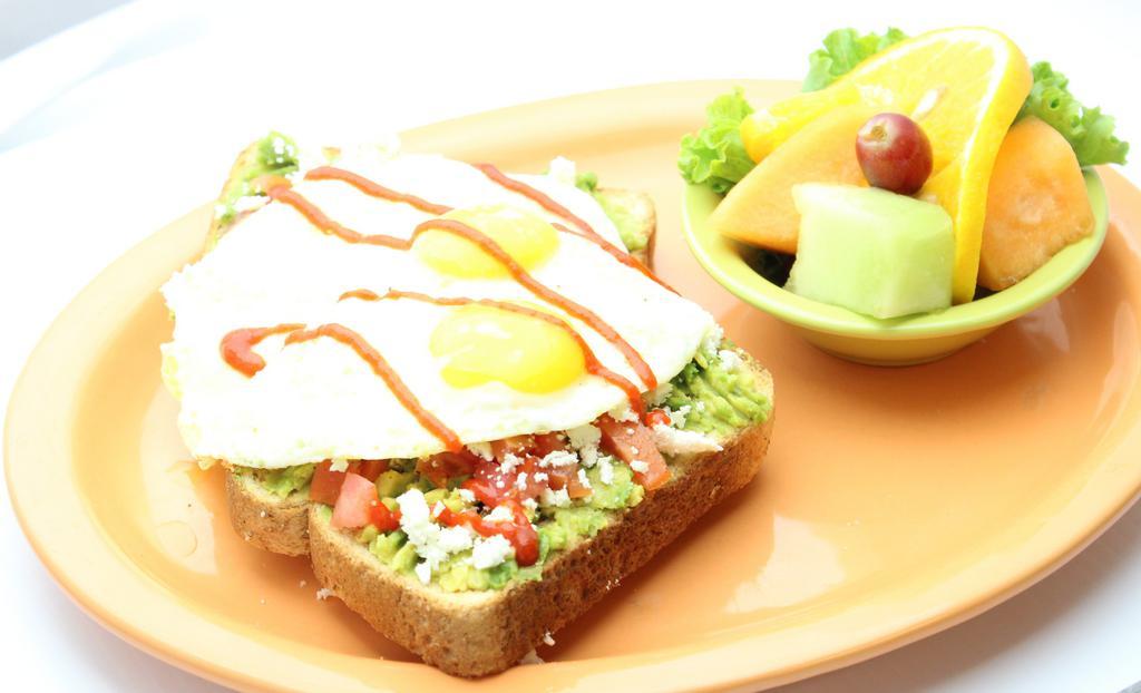 Avocado Toast · Avocado lovers rejoice! Our breakfast spin on a delicious new trend; wheat toast covered in mashed avocados, diced tomatoes, feta cheese, and two sunny-side-up eggs. Sprinkled with our signature spices and drizzled in sriracha sauce. Served with a scrambler side.