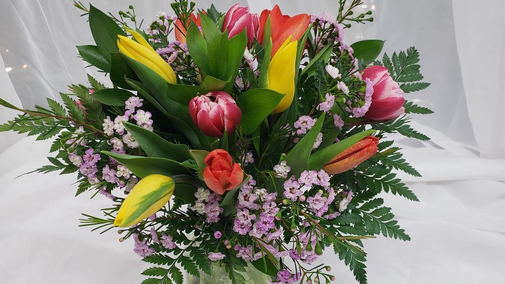 Spring Tulips · A dozen mixed tulips designed with mixed greens and wax flower in a beautiful clear glass vase.