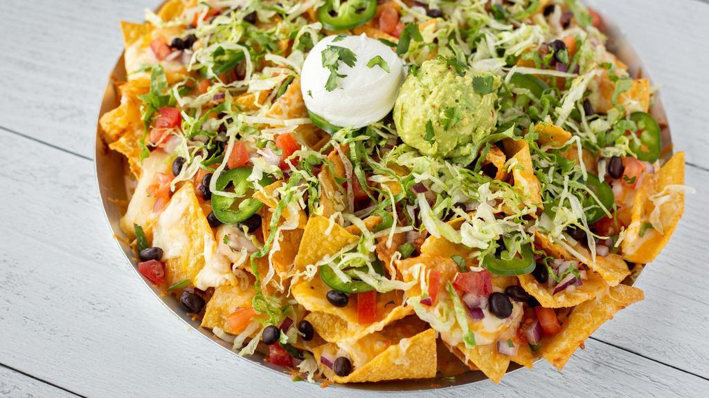 Knock-Out Nachos · Crisp tortilla chips with white Cheddar queso, melted Cheddar and Habanero Jack. Topped with fresh pico de gallo, black beans, tomatoes, fresh jalapeños, shredded lettuce, sour cream, guacamole, and cilantro.