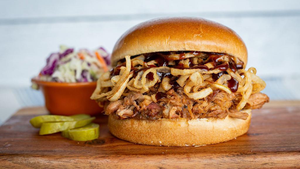 Bbq Pulled Pork · Slow-smoked pork tossed in BBQ sauce, piled high with crispy onion straws on a brioche bun & served with a side of coleslaw.