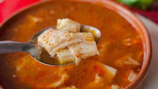 Menudo · Traditional Mexican soup made with beef tripe in broth with red chili pepper base, hominy, lime, chopped onions, chile de árbol, Valentina and crushed oregano