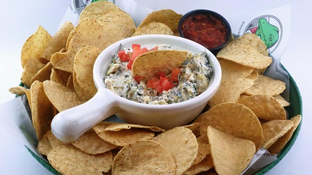 Spinach & Artichoke Dip · A creamy blend of chopped spinach, tender artichoke hearts, and Parmesan cheese. Topped with diced tomatoes and served with warm tortilla chips and salsa.