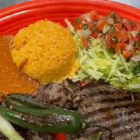 Carne Asada · Grilled beef steak served with rice, beans, salad, a jalapeño pepper, and knob onions.