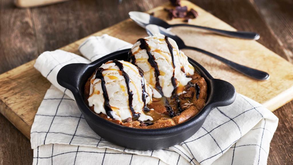 Chocolate Chip Cookie Skillet · A freshly baked chocolate chip cookie served warm in a skillet with vanilla bean ice cream and drizzled with caramel and chocolate sauces. It’s enough to share… or not!