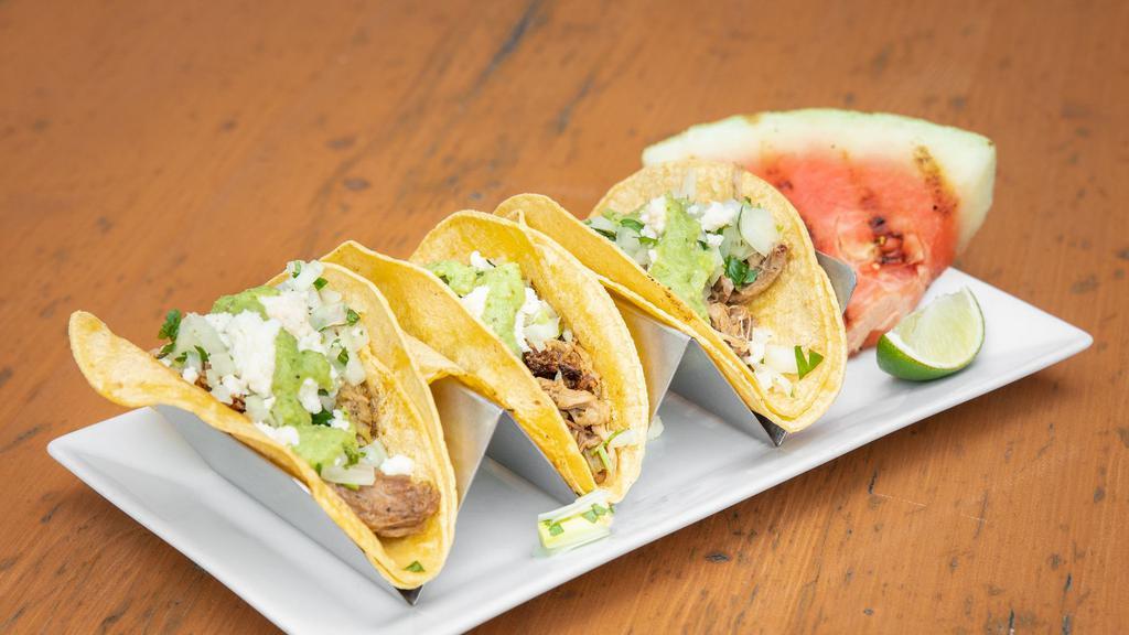Carnitas · Corn tortillas, Absolution Amber pulled pork, onion, cilantro, salsa Verde, Queso fresco.  Served with a wedge of grilled watermelon.