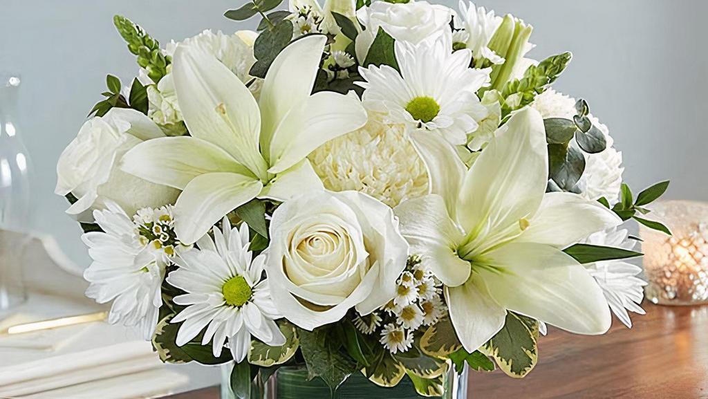 Healing Tears All White · Our sympathy arrangement of angelic white roses, lilies, mums, daisy poms and more, expertly arranged in a clear glass cube lined with a Ti leaf ribbon, makes for an exquisite gesture of comfort and healing.
Medium arrangement measures approximately 10