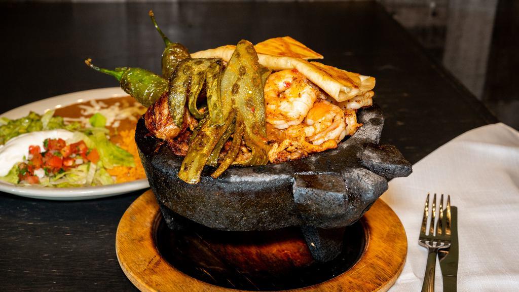 Molcajetes De Camaron · Shrimp, tilapia, jalapeños, onions, bell peppers, nopales, queso fresco, rice, beans, and a guacamole salad, served with a side of flour tortillas.